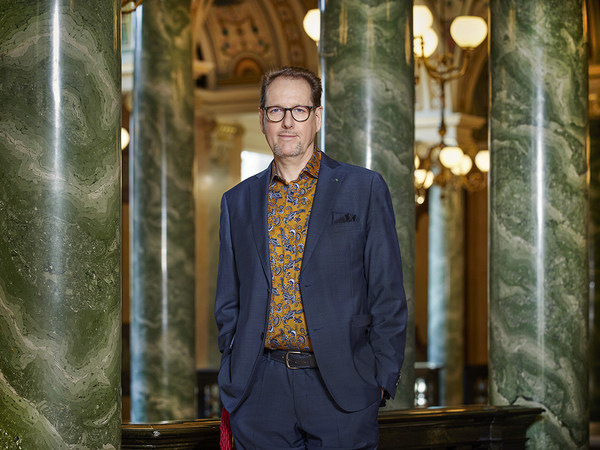 Mann in blauem Anzug steht im Foyer der Semperoper vor grün marmorierten Säulen